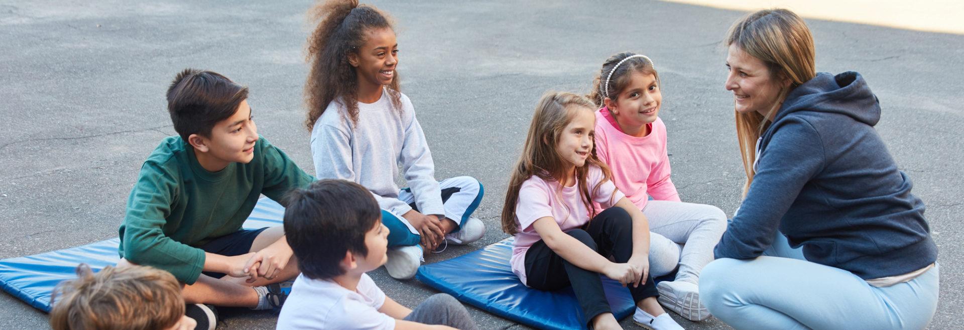 孩子们坐在瑜伽垫上听教练讲课